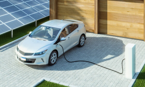 Ein Elektroauto hängt an einer Ladesäule vor einer Garage. Zudem sind auf dem Bild mehrere Solarmodule zu sehen.