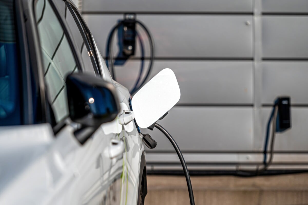 Ein Elektroauto steht vor einer Garage und ist mit einem Ladekabel mit einer Lademöglichkeit verbunden.