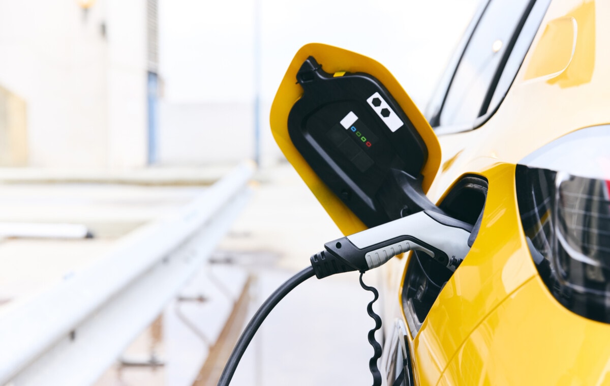 Ein Ladestecker steckt in einem gelben Elektroauto vor einem sehr weißen und hellen Hintergrund.
