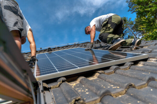 Zwei Arbeiter installieren ein Solarmodul auf einem Dach