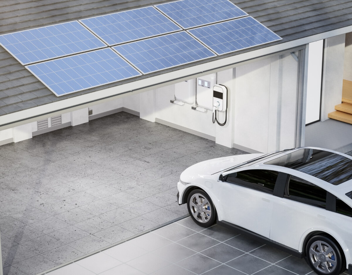 Ein Elektroauto parkt vor einer Garage in der eine Ladeeinrichtung und ein Stromspeicher zu sehen ist. Auf dem Dach ist eine Solaranlage bzw. Pv-Anlage montiert.